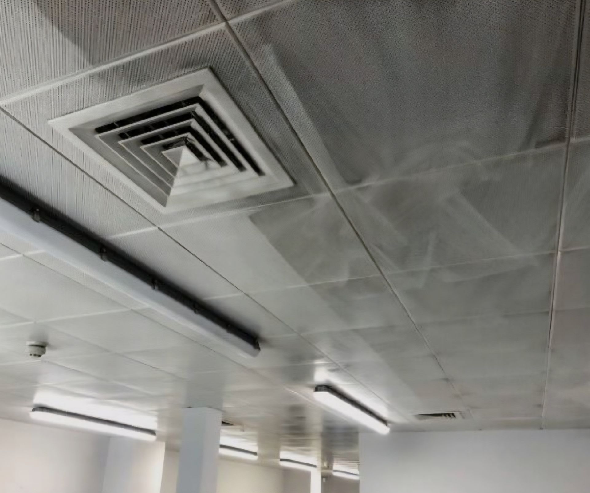 Un falso techo con placas cuadradas de metal sucias y una rejilla de ventilación cuadrada para el sistema de climatización.