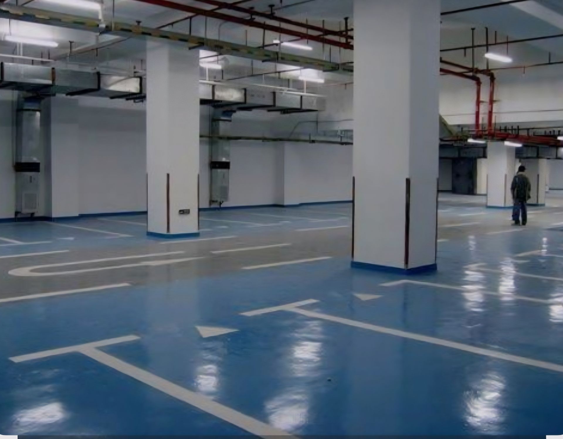 Suelo garaje con aparcamientos pintados en el suelo de azul y la mitad pintada de gris con columnas blancas y marcas