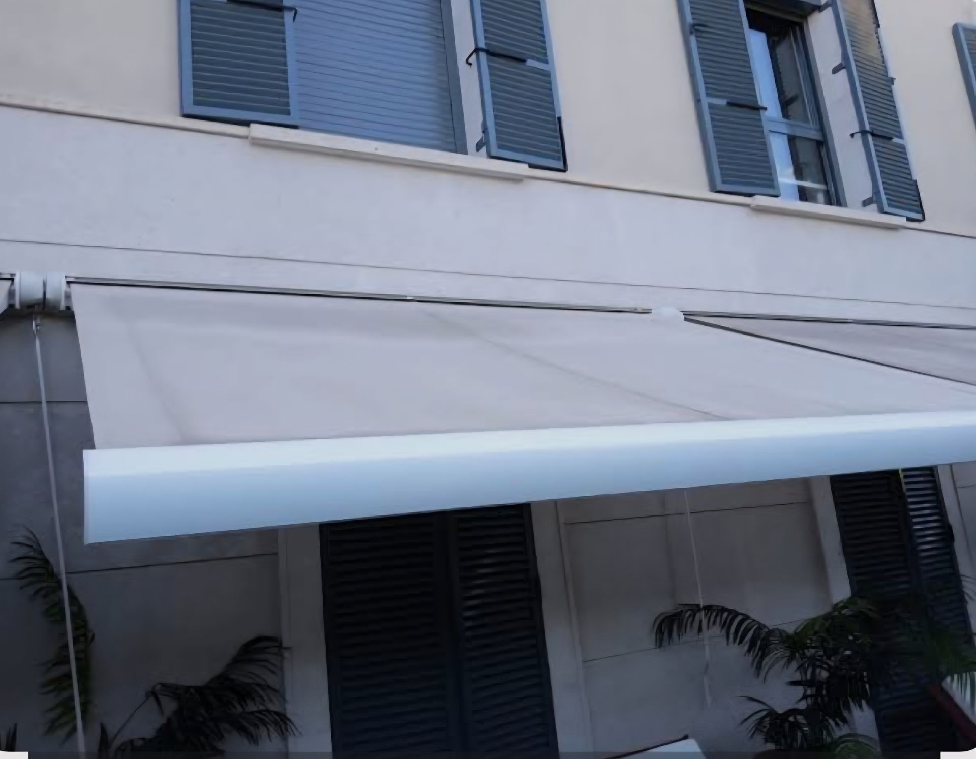 Un toldo retráctil de color beige se extendía sobre la fachada de un edificio con contraventanas oscuras y vegetación.