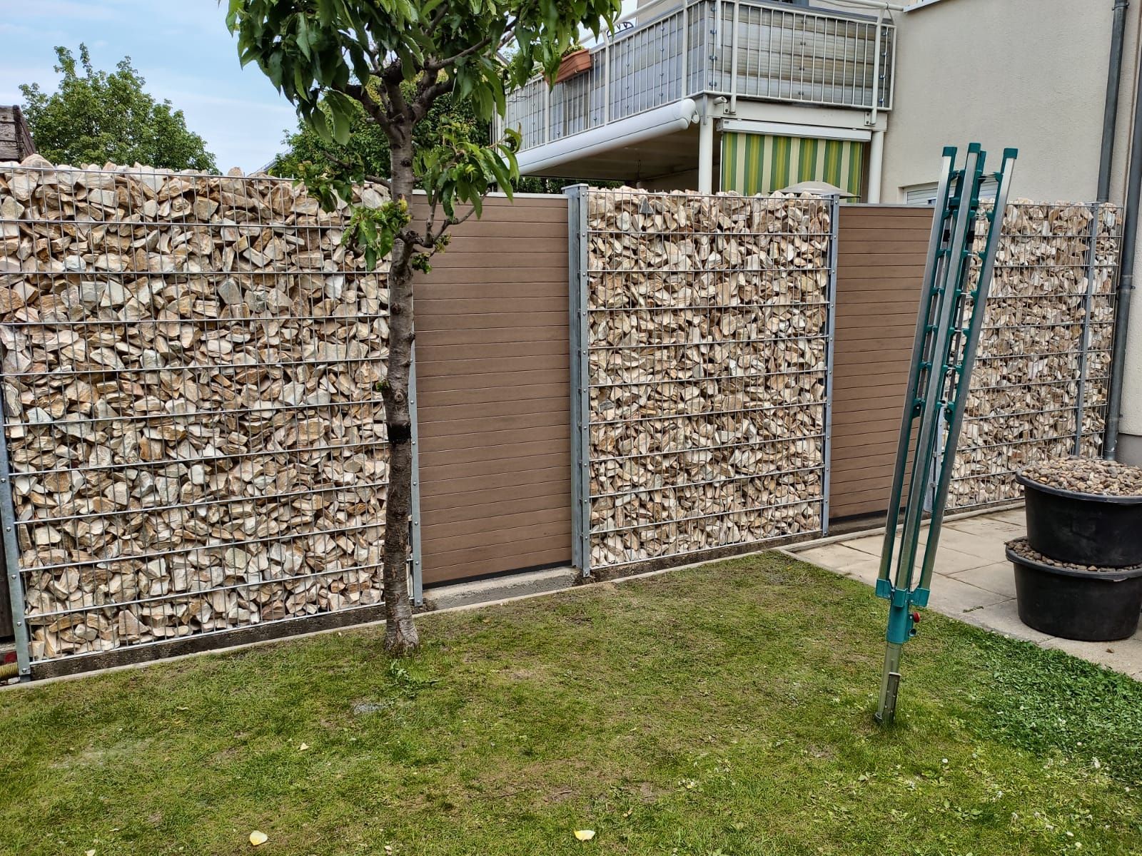 Sichtschutzzaun aus Gabionen und Holz in einem Hinterhof mit einem Wäscheständer.