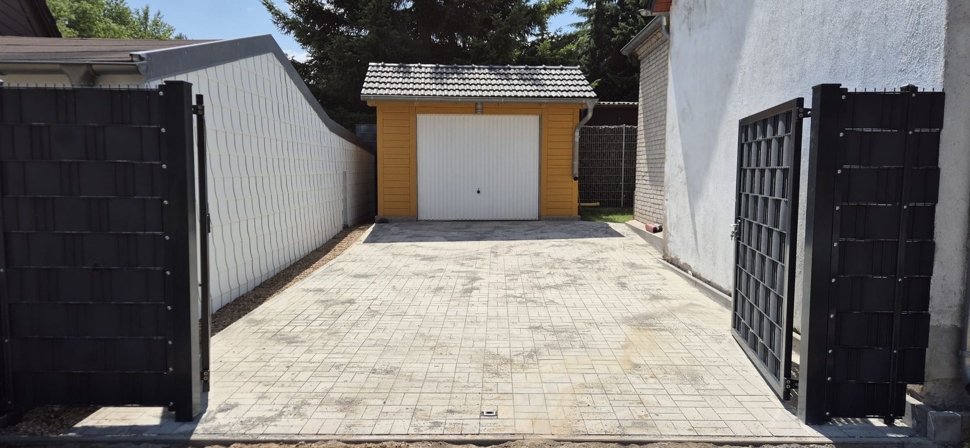Eine Auffahrt führt zu einer gelben Garage mit einem weißen Tor, flankiert von schwarzen Toren und einer weißen Wand.