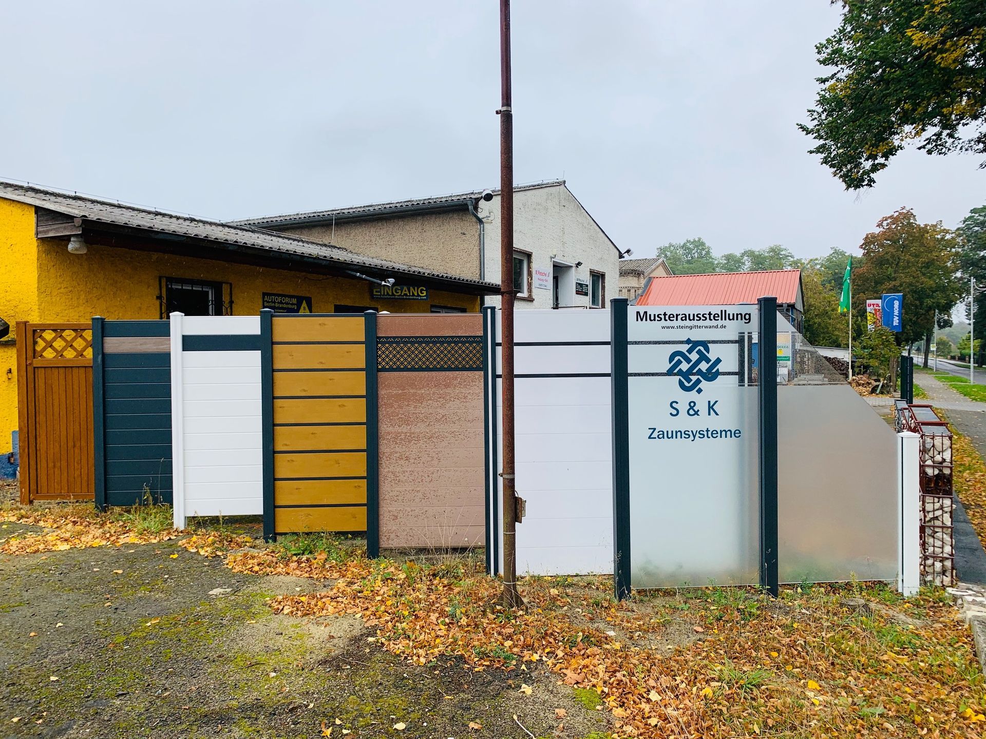 Vor einem Gebäude sind verschiedene Zaunmuster in unterschiedlichen Farben, Texturen und Designs ausgestellt. Bewölkter Himmel.