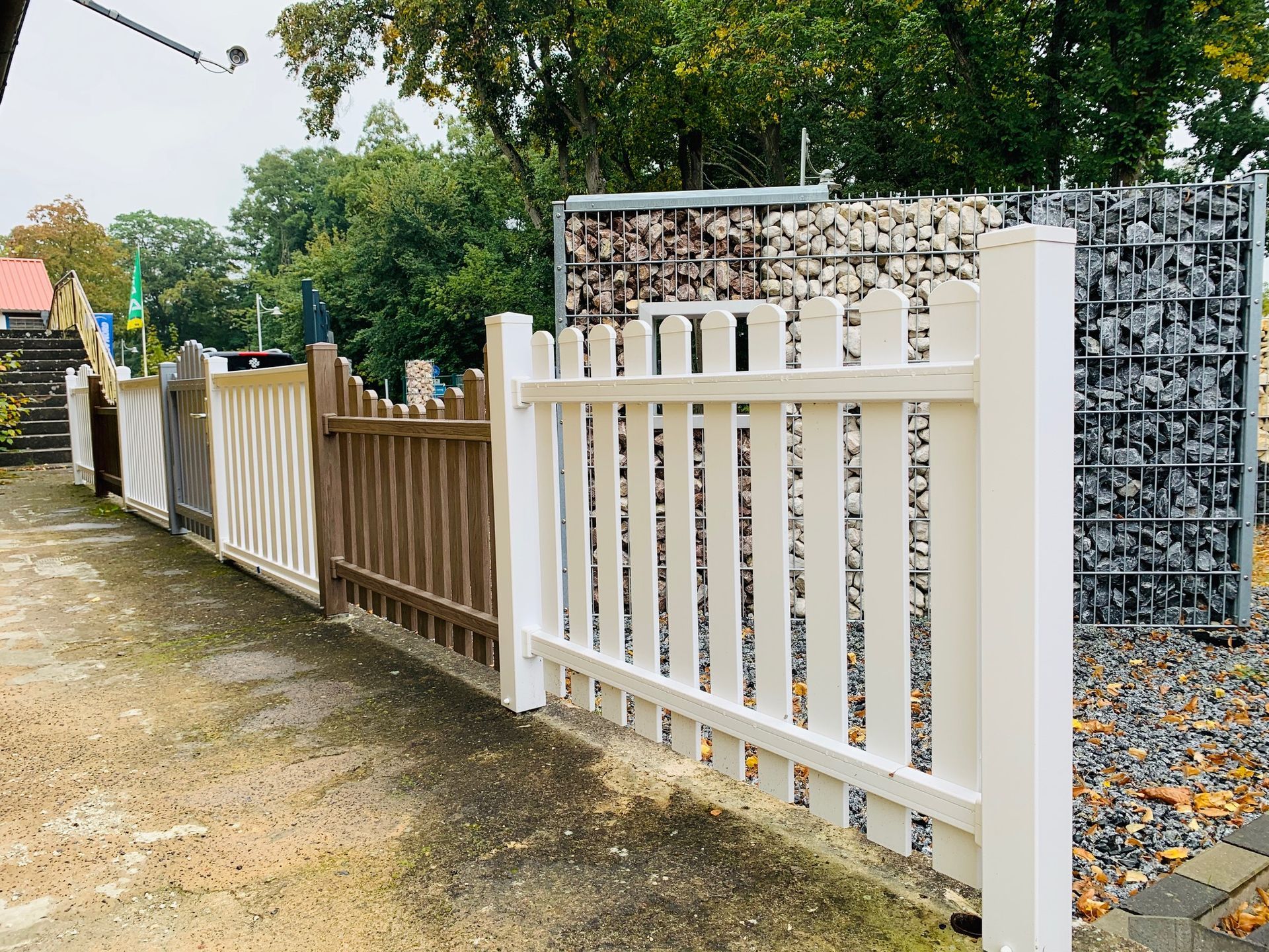 Draußen ist eine Reihe verschiedener Zaunstile zu sehen: Weiß, Braun und Beige mit unterschiedlichen Lattenmustern.