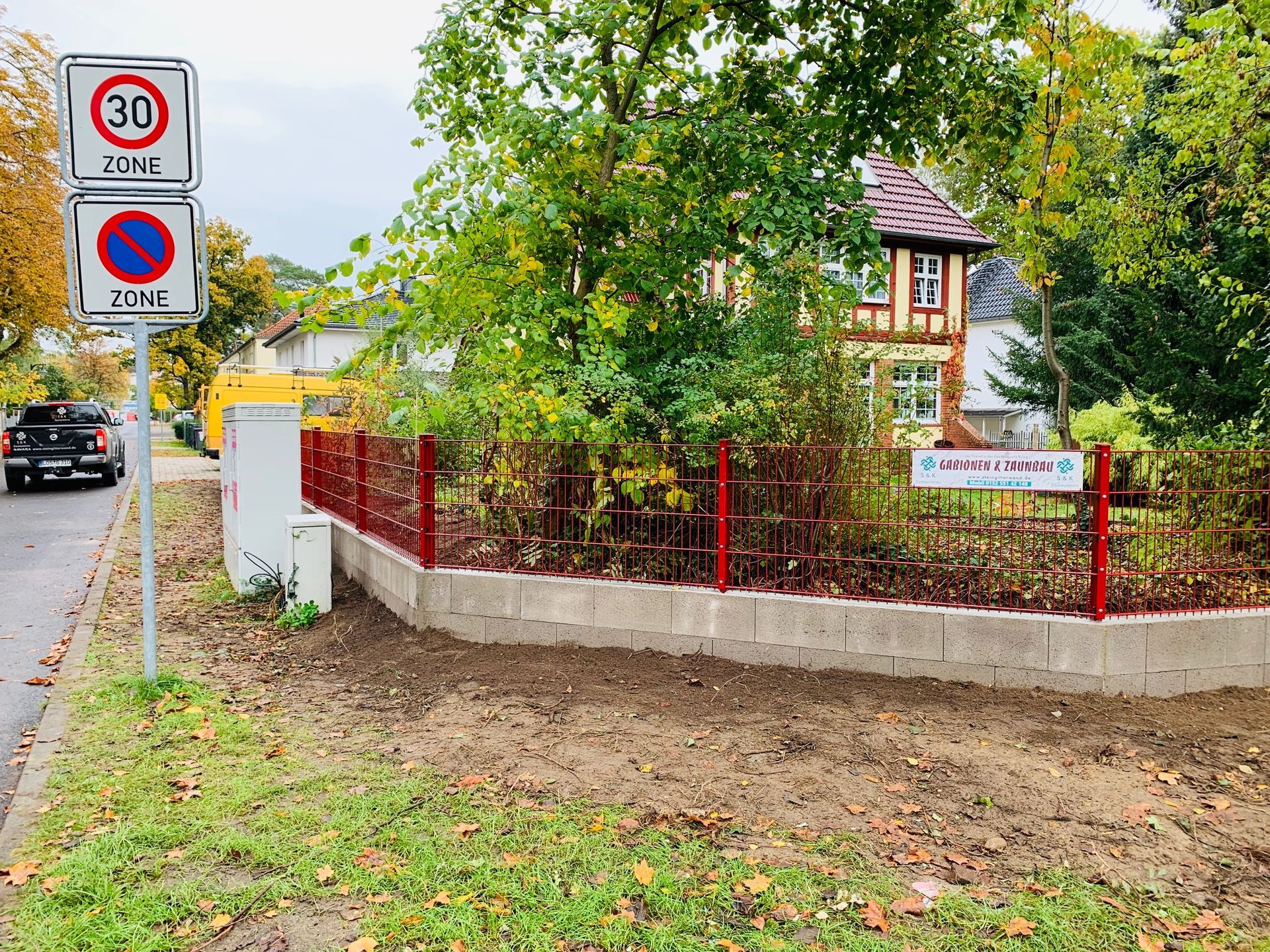 Straßenszene mit Tempo-30-Schild. Roter Zaun umgibt ein Gebäude mit einem Schild mit der Aufschrift „Kindertagesstätte“.