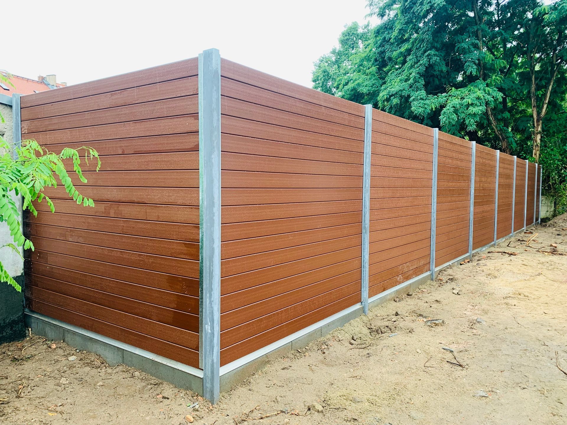 Brauner horizontaler Lattenzaun mit silbernen Metallpfosten, im Freien.