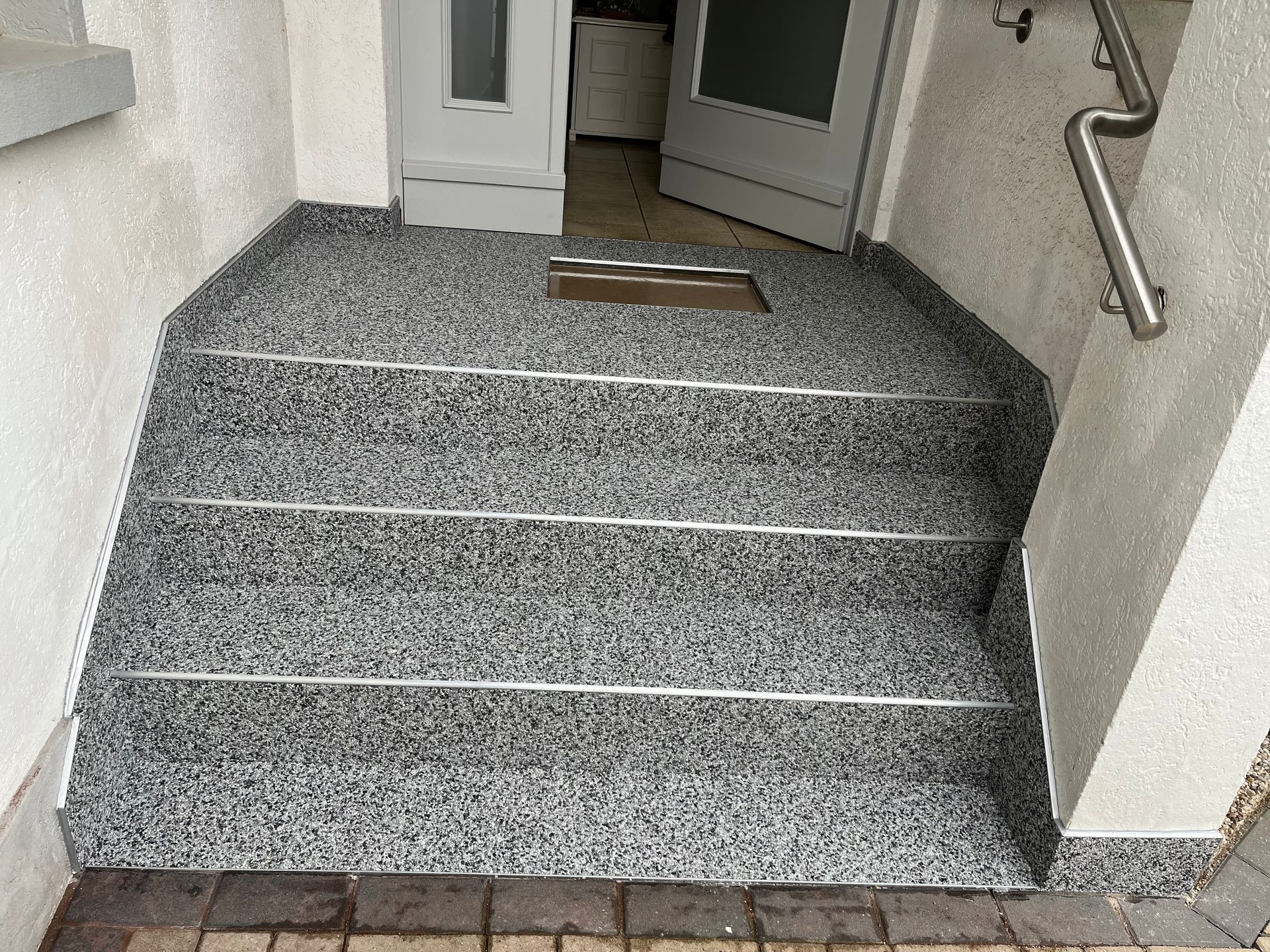 Stufen führen zu einer Tür, bedeckt mit gesprenkeltem grauem Material mit silbernen Akzenten. Auf der rechten Seite befindet sich ein Metallhandlauf.