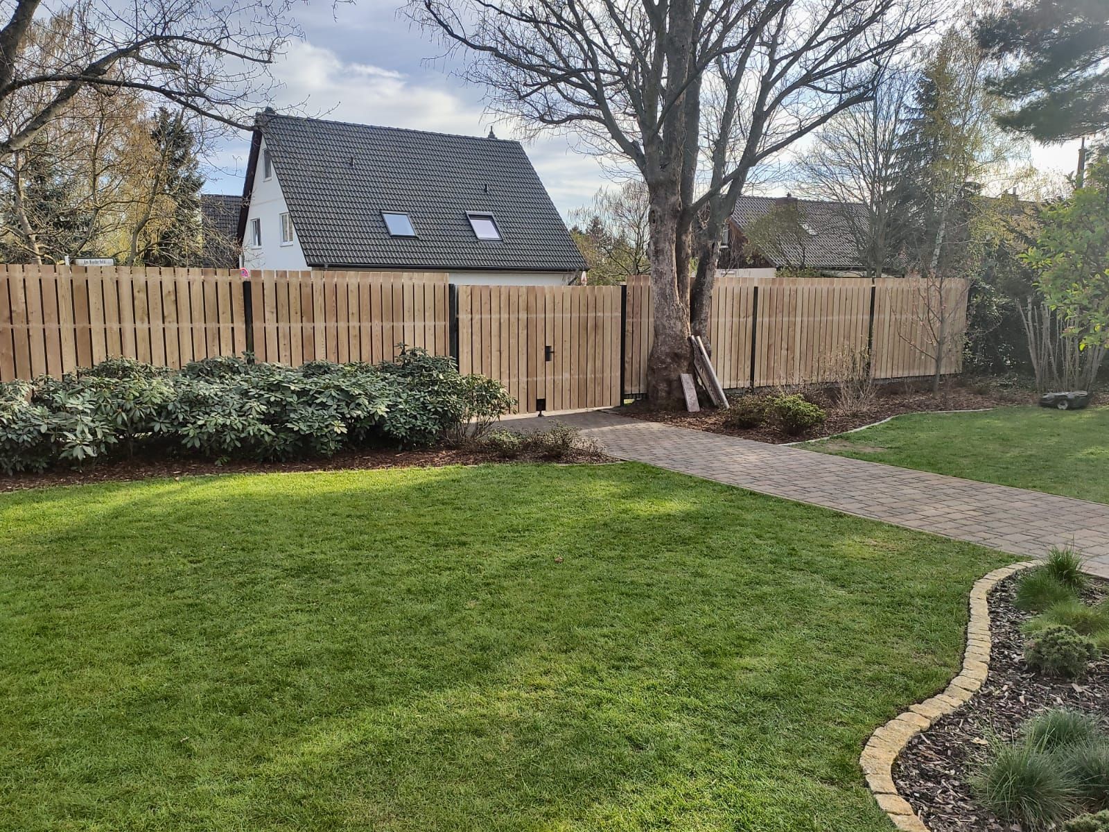Ein Holzzaun umgibt einen Hinterhof mit grünem Gras, einem Steinweg und einem Haus im Hintergrund.