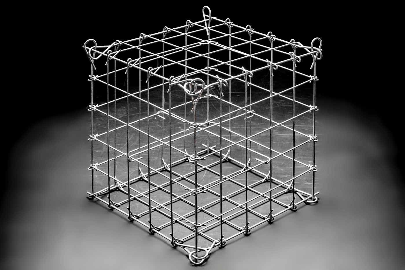 Ein Drahtgitterwürfel in Graustufen. Es handelt sich um eine symmetrische Gitterstruktur mit Schleifen an den oberen und unteren Ecken vor einem dunklen Hintergrund.