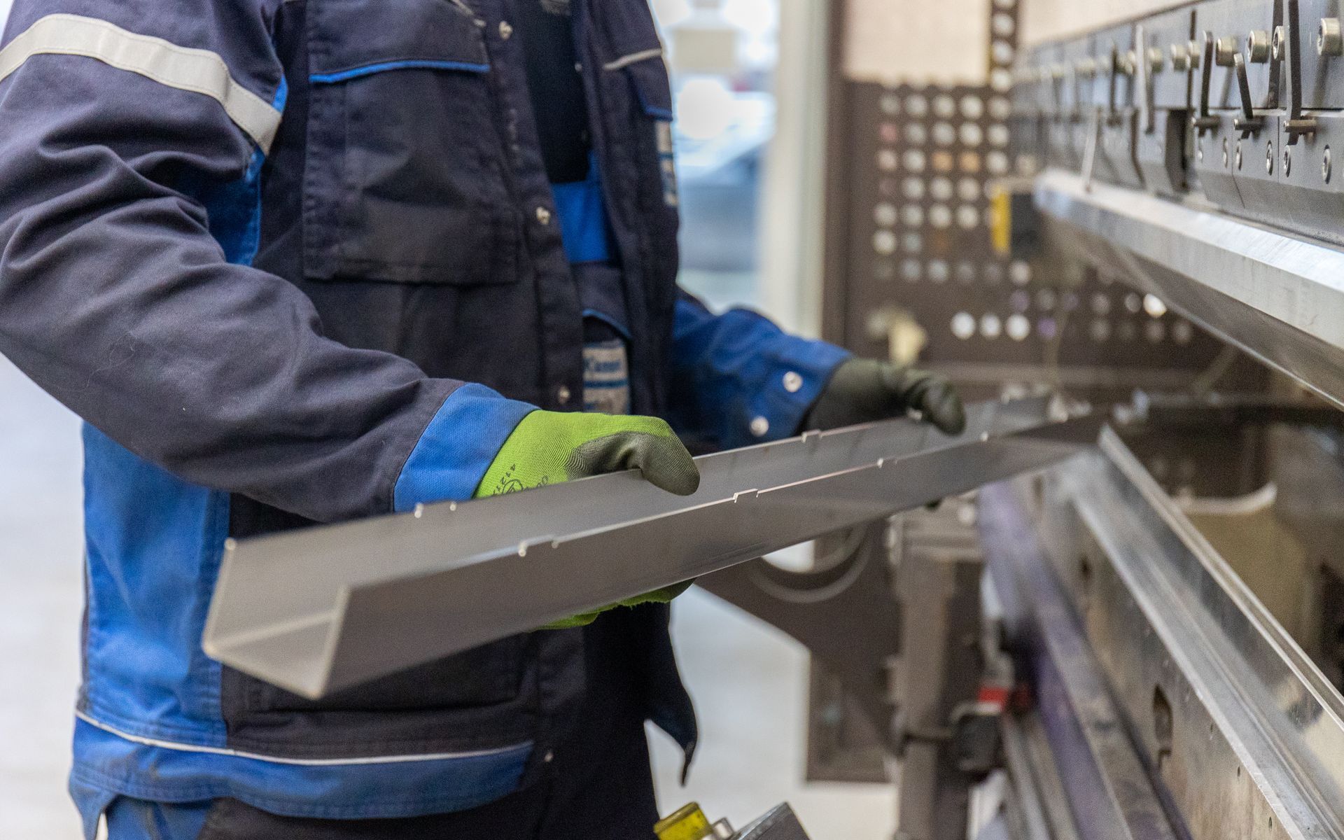 Ein Mann arbeitet in einer Fabrik an einer Maschine und hält ein Stück Metall in der Hand.