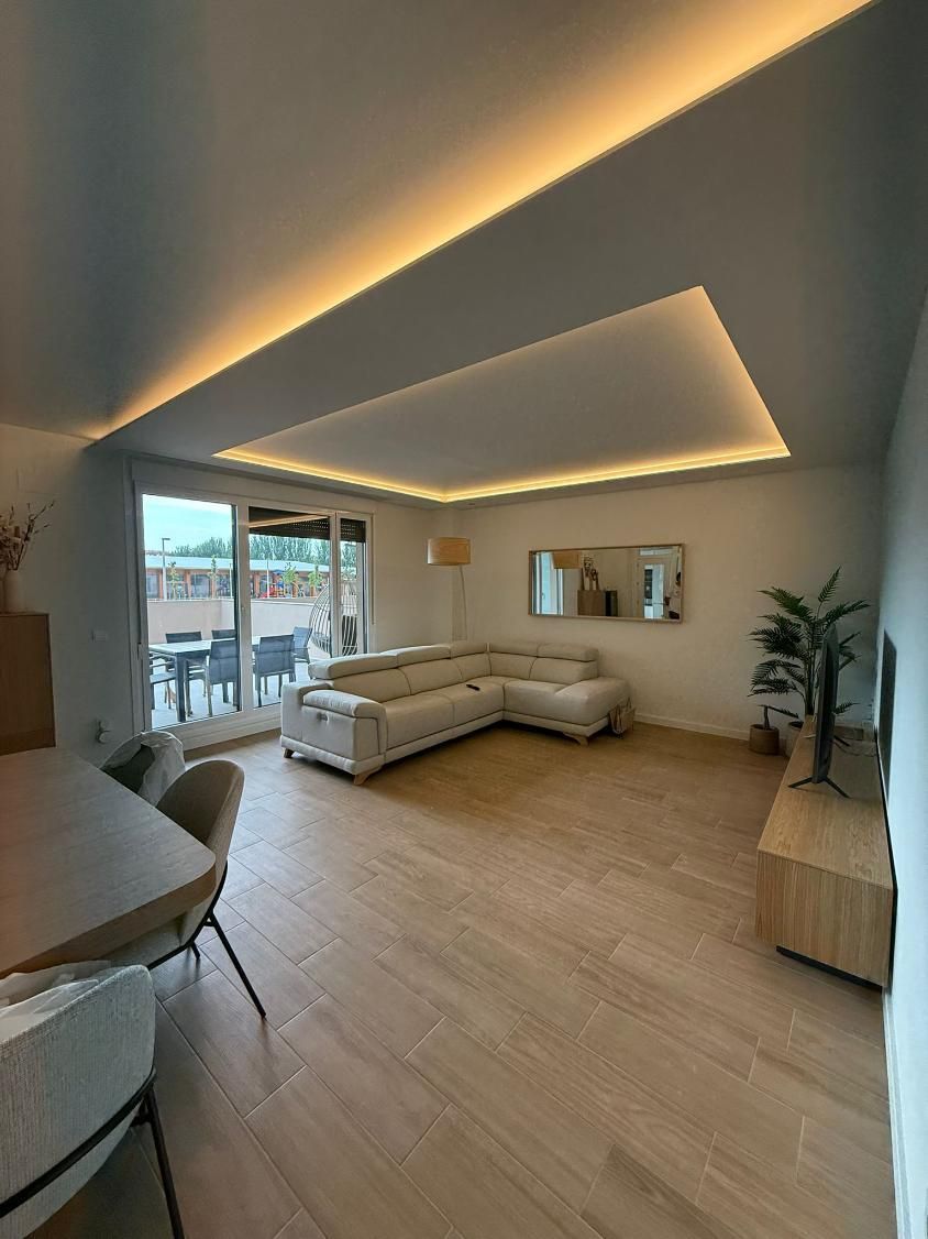 Sala de estar moderna con pisos de colores claros, sofá seccional beige e iluminación empotrada en el techo.