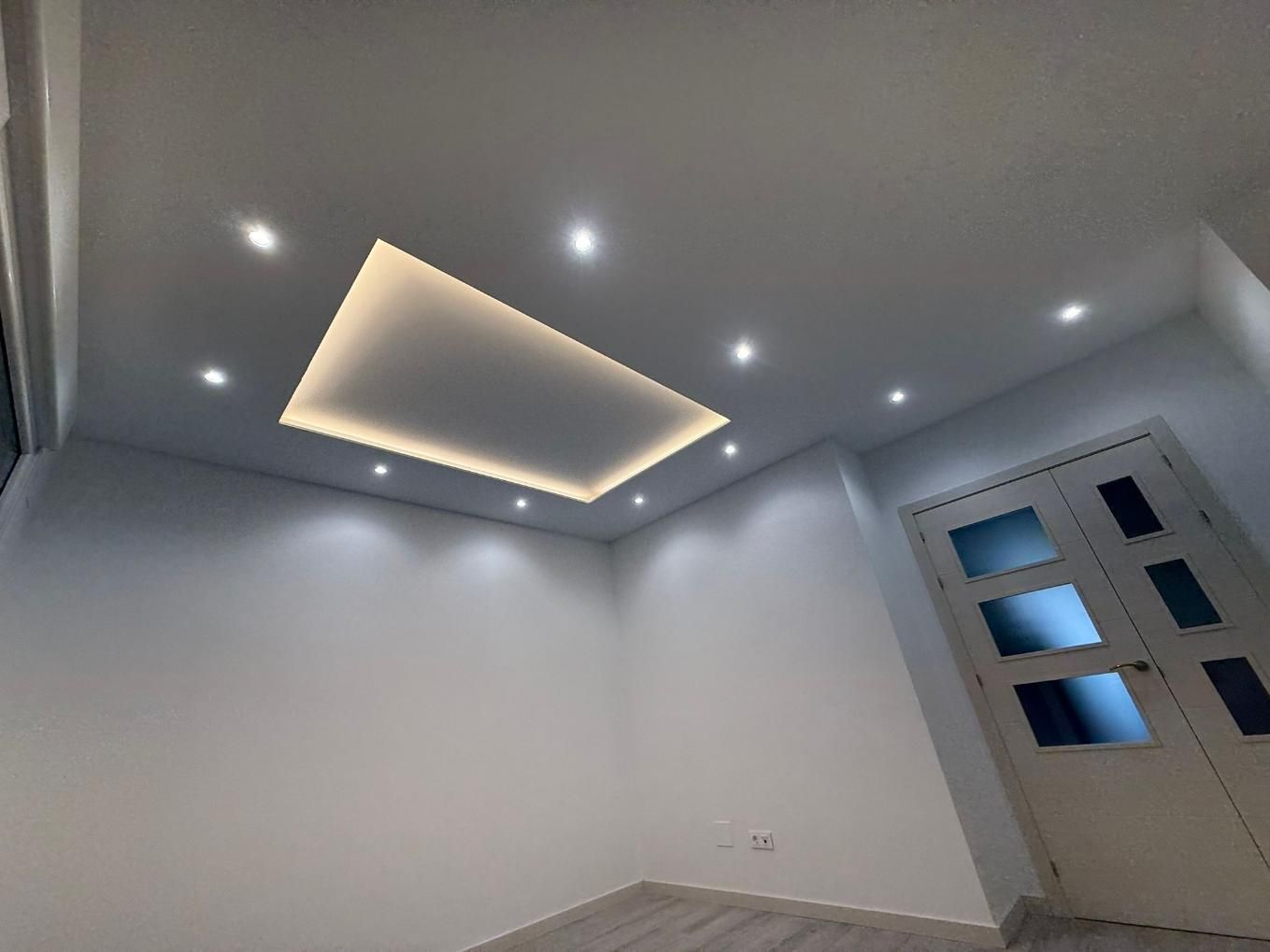 Habitación vacía con luces empotradas en el techo y un panel rectangular iluminado.