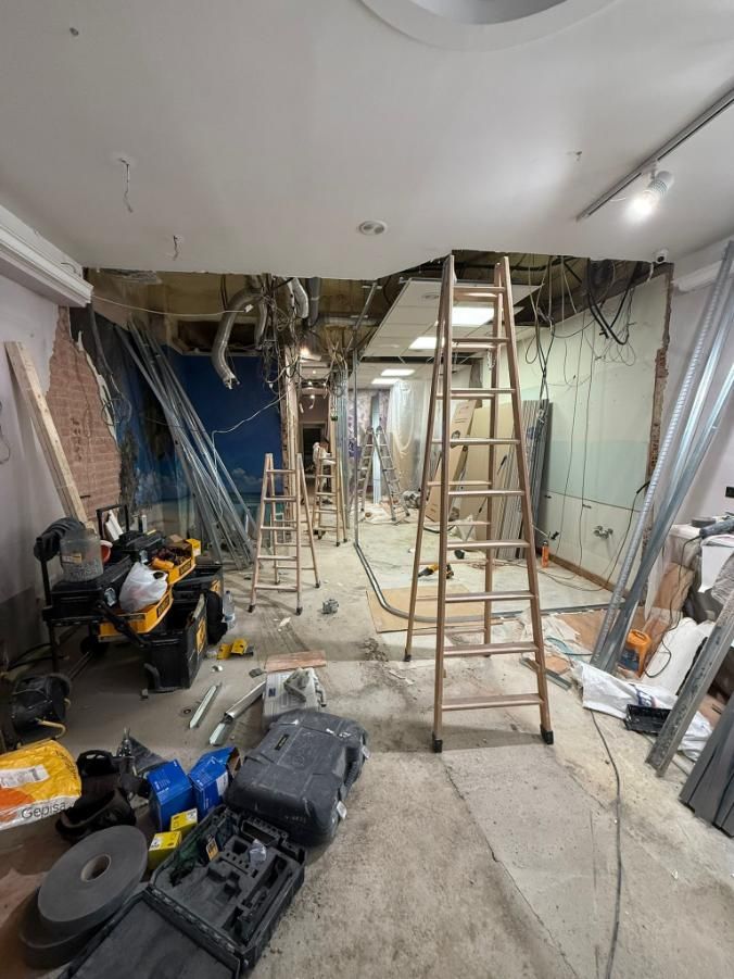 Interior de un edificio en remodelación, con escaleras, herramientas, cableado expuesto y paredes parcialmente demolidas.