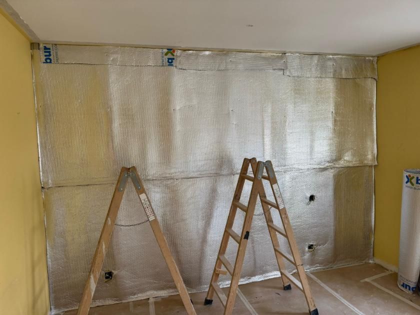 Habitación con una pared parcialmente aislada; dos escaleras se apoyan en ella.