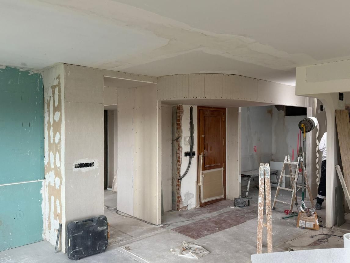 Interior de una habitación en construcción, con paneles de yeso expuestos, paredes sin terminar y equipo de construcción.