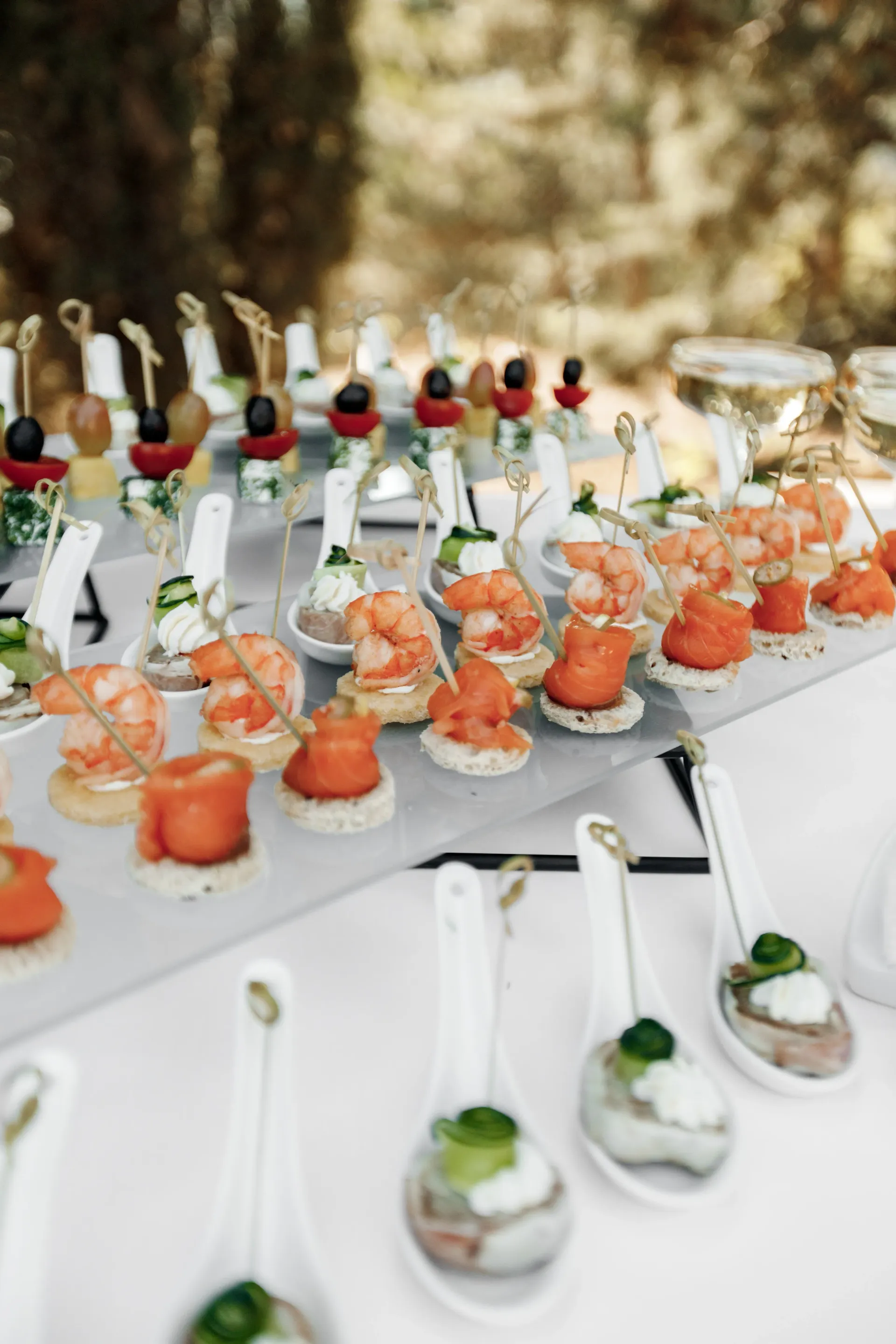 Aperitivos en mesa de buffet: camarones, salmón y otros pequeños bocados en cucharas y brochetas.