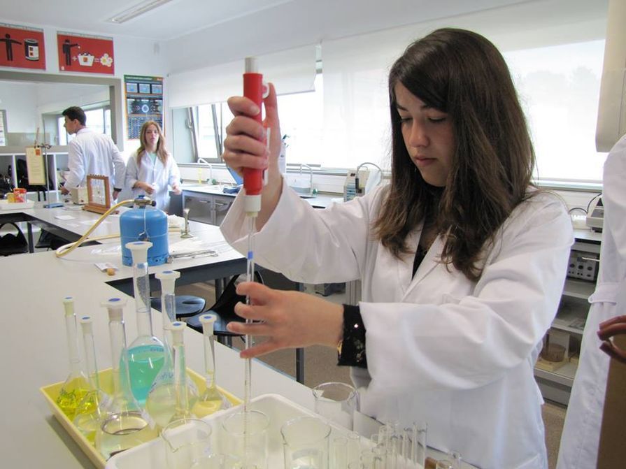 Jovem de jaleco branco usando uma pipeta com tubos de ensaio em um ambiente de laboratório.