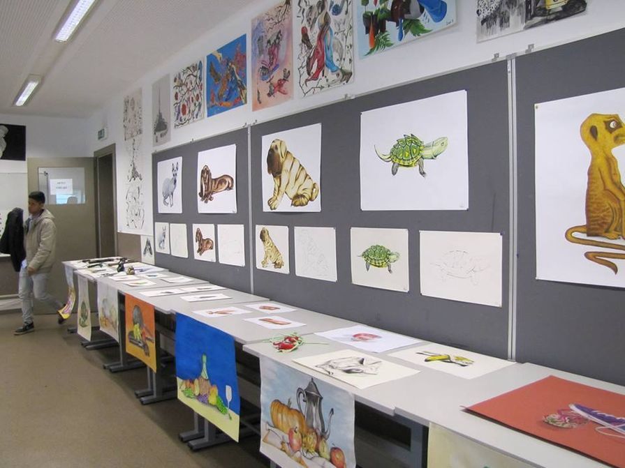 Exposição de obras de arte em uma galeria; pinturas de animais e paisagens em exibição.