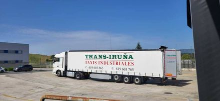 Camión blanco de caja cerrada Trans-Iruna estacionado en un soleado lote industrial con otros remolques cerca.