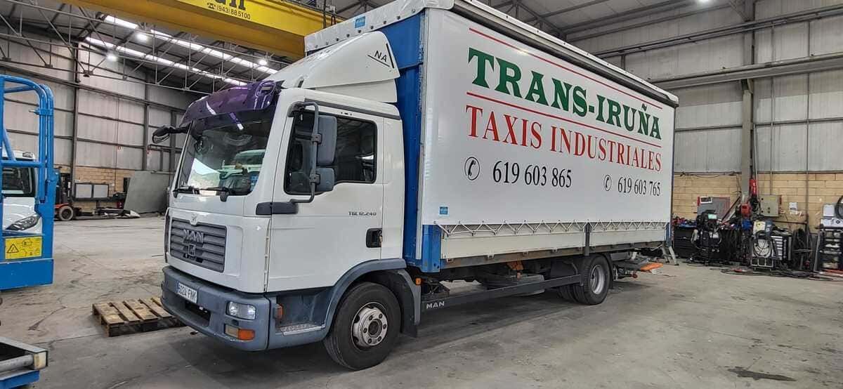 Camión de reparto blanco con texto rojo estacionado dentro de un almacén industrial.