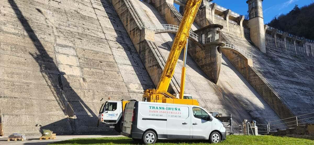 Una furgoneta blanca y una grúa amarilla trabajan contra un gran muro de contención de hormigón.
