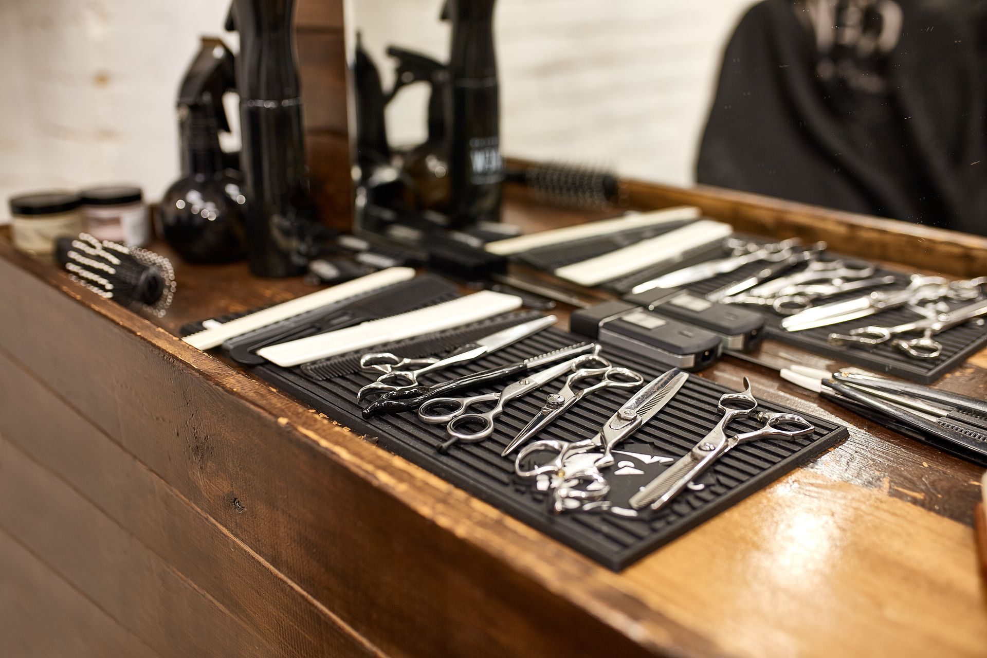 Outils de barbier sur un comptoir en bois : ciseaux, peignes, vaporisateurs et contenants de produits capillaires.