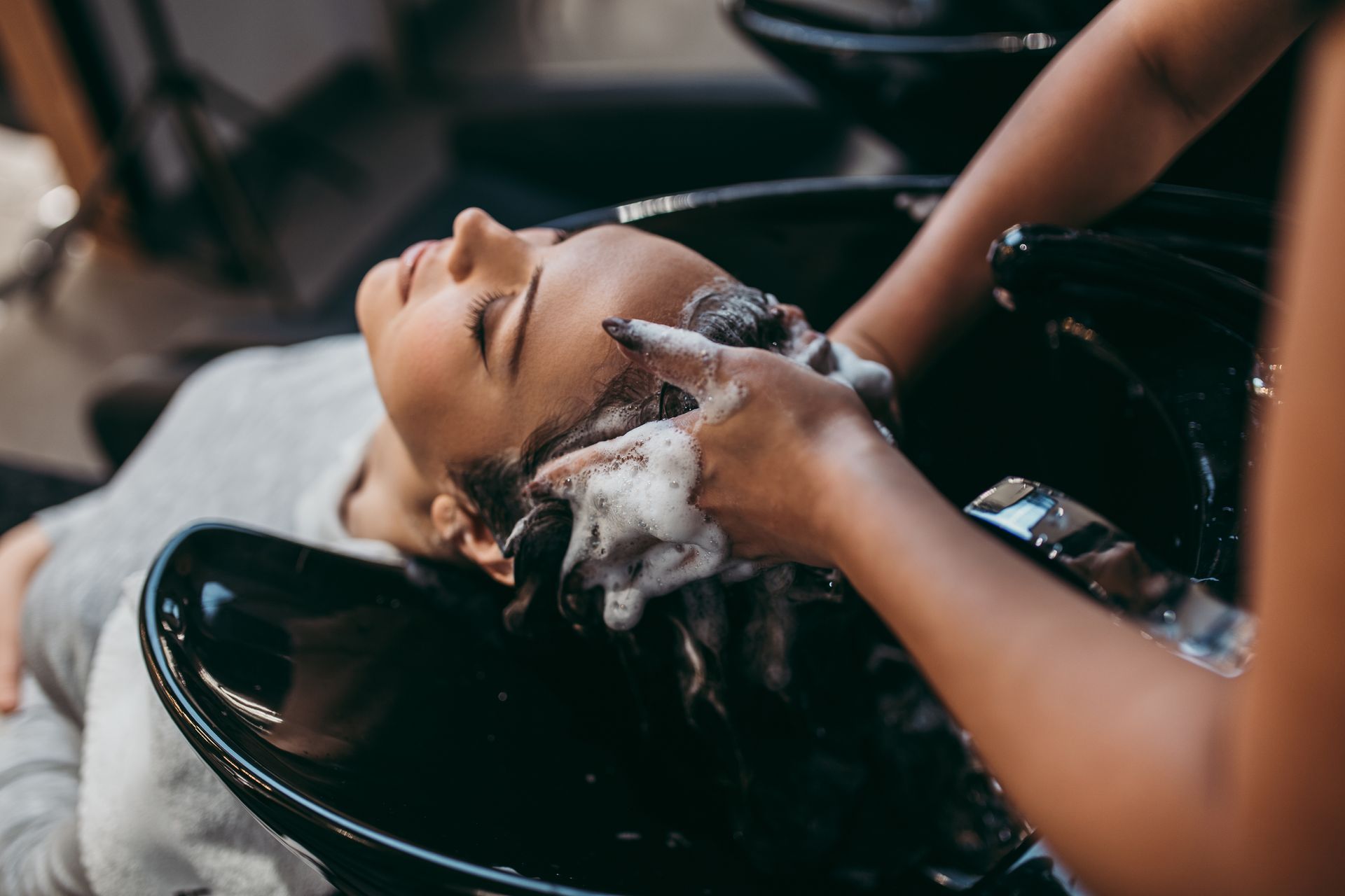 Une femme se fait laver les cheveux dans un salon, avec du shampoing sur les cheveux.