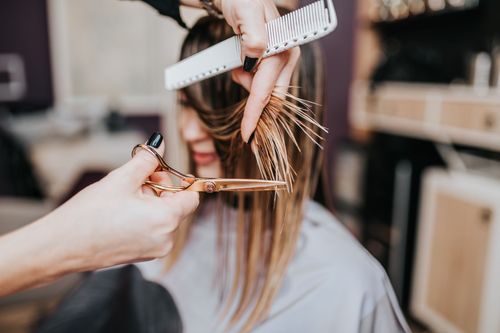 Coiffeur coupant la frange d'une femme avec des ciseaux et un peigne dans un salon de coiffure.