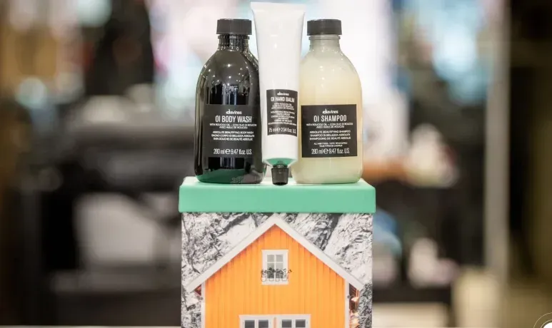 Coffret cadeau comprenant trois bouteilles et un tube sur une boîte en forme de maison ; maison orange, bouteilles noires, tube blanc.