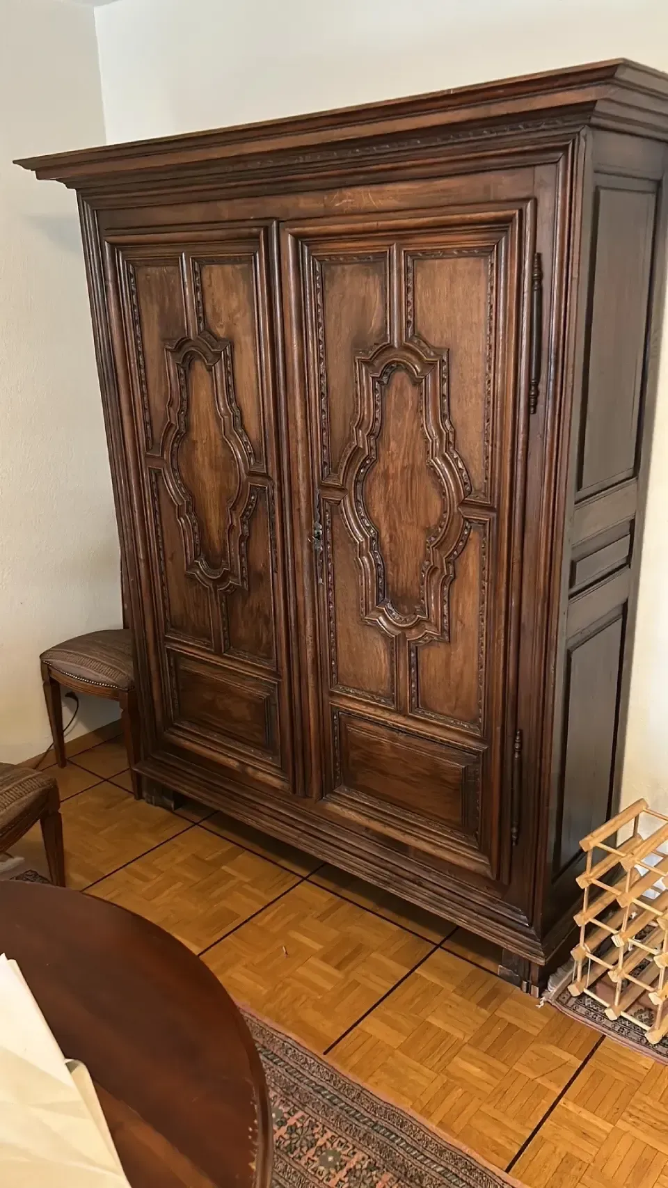 A large wooden wardrobe is sitting in a living room next to a rug.