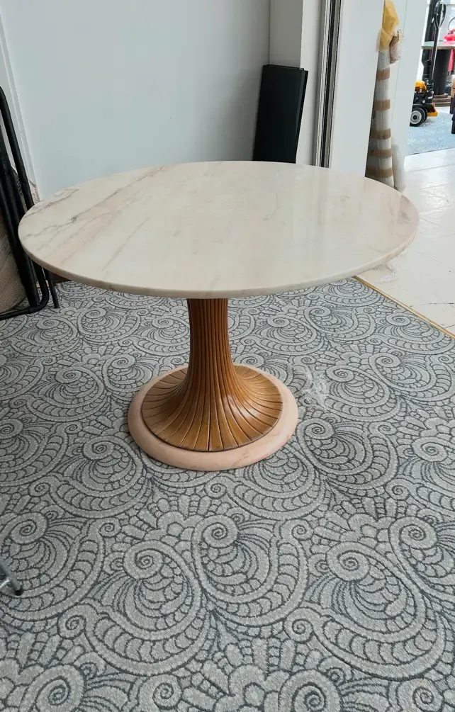 A round table with a wooden base is sitting on a tiled floor.