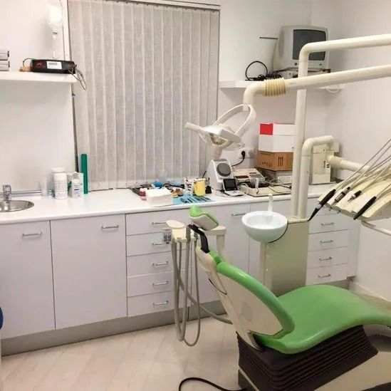 Un consultorio dental con una silla verde y gabinetes blancos.