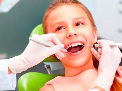 A una niña le están examinando los dientes un dentista.