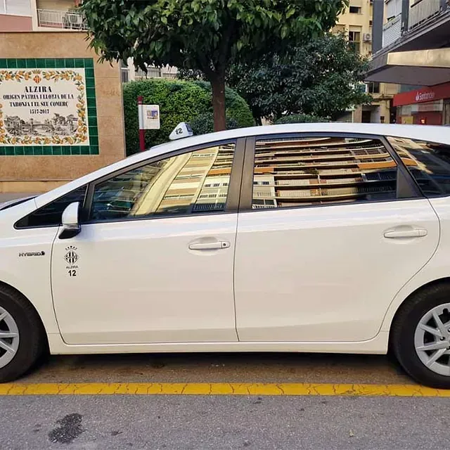 Un coche blanco está aparcado delante de un cartel que dice alzira