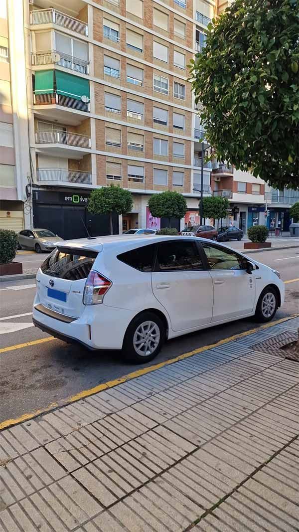 Un coche blanco está estacionado al costado de la carretera frente a un edificio.