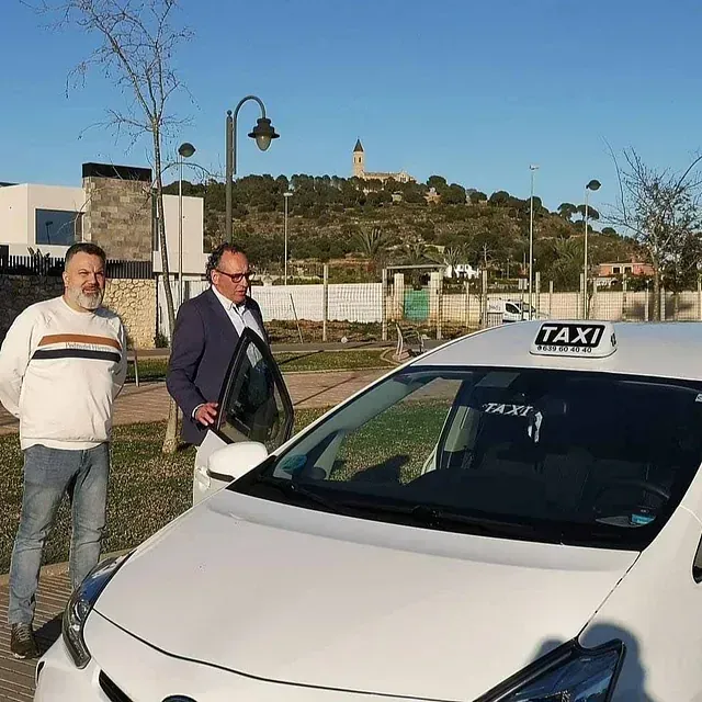 Dos hombres están parados junto a un taxi blanco.