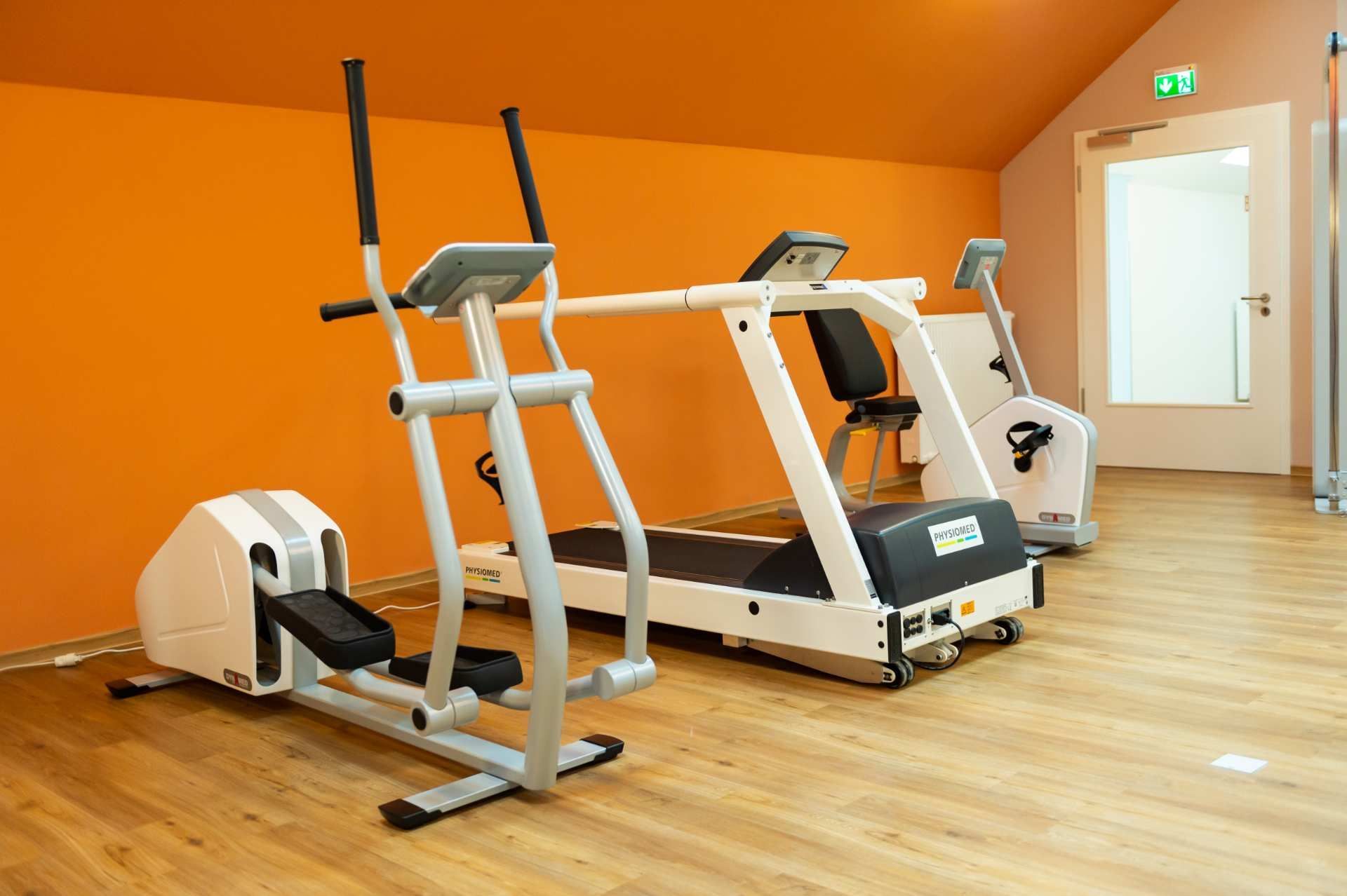 Trainingsbereich mit zwei Fitnessgeräten vor orangefarbener Wand.