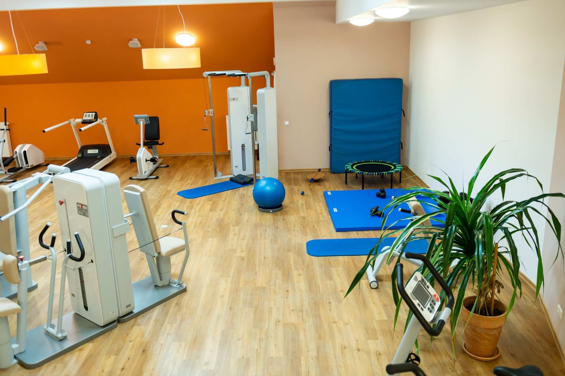 Fitnessraum mit orangefarbener Wand, Trainingsgeräten und Gymnastikbällen.