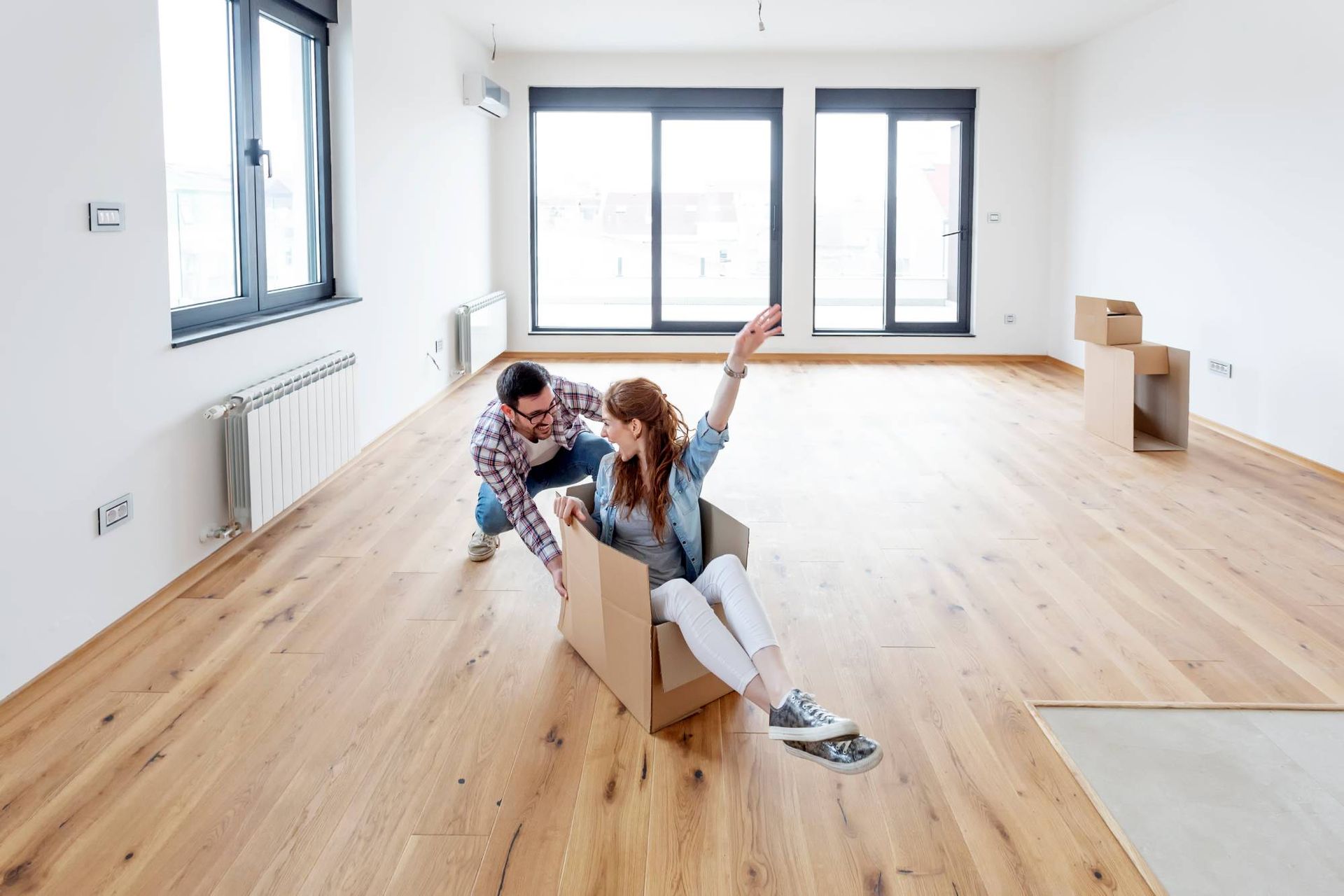 Un homme et une femme jouent avec une boîte en carton dans une pièce vide.
