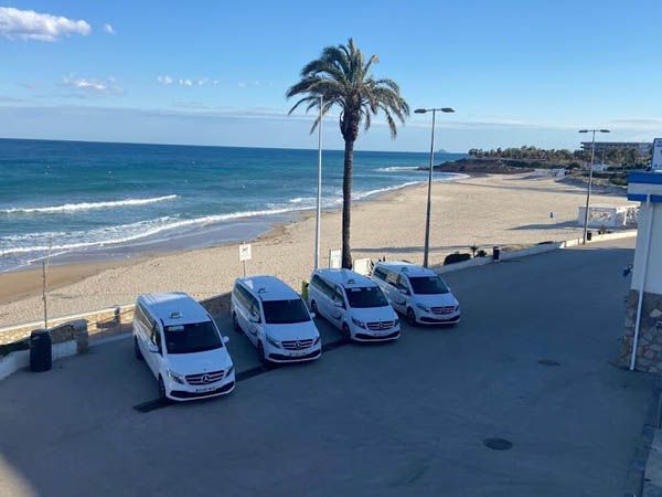 Una fila de furgonetas blancas están estacionadas frente a una playa.