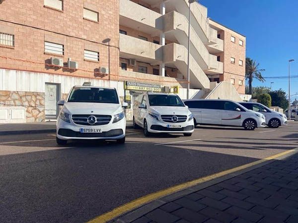 Tres furgonetas blancas están estacionadas al costado de la carretera frente a un edificio.