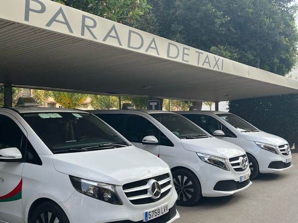 Una fila de camionetas blancas estacionadas bajo un cartel que dice parada de taxi