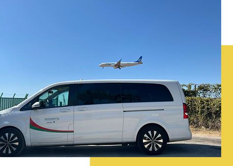 Una camioneta blanca está estacionada frente a un avión que vuela en el cielo.