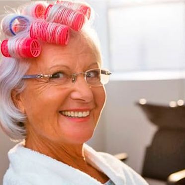 Una mujer con rulos en el pelo está sonriendo y usa gafas.