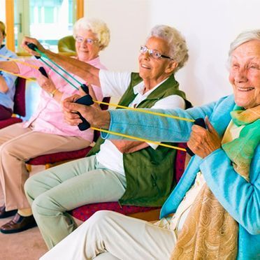 Un grupo de mujeres mayores están sentadas en sillas haciendo ejercicios con bandas de resistencia.