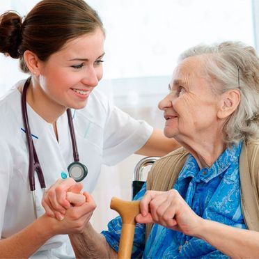 Una enfermera sostiene la mano de una anciana en silla de ruedas.