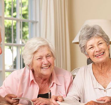 Dos mujeres mayores están sentadas en una mesa con un hombre y sonríen.