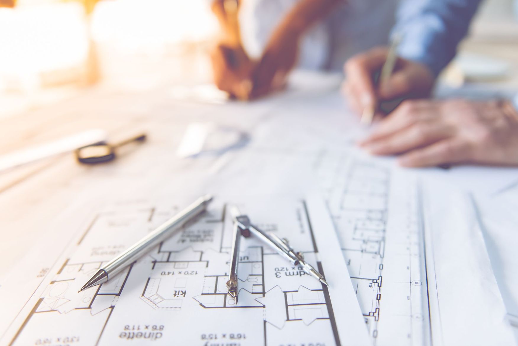 Plans architecturaux avec des mains dessinant une maquette de maison sur un bureau lumineux.
