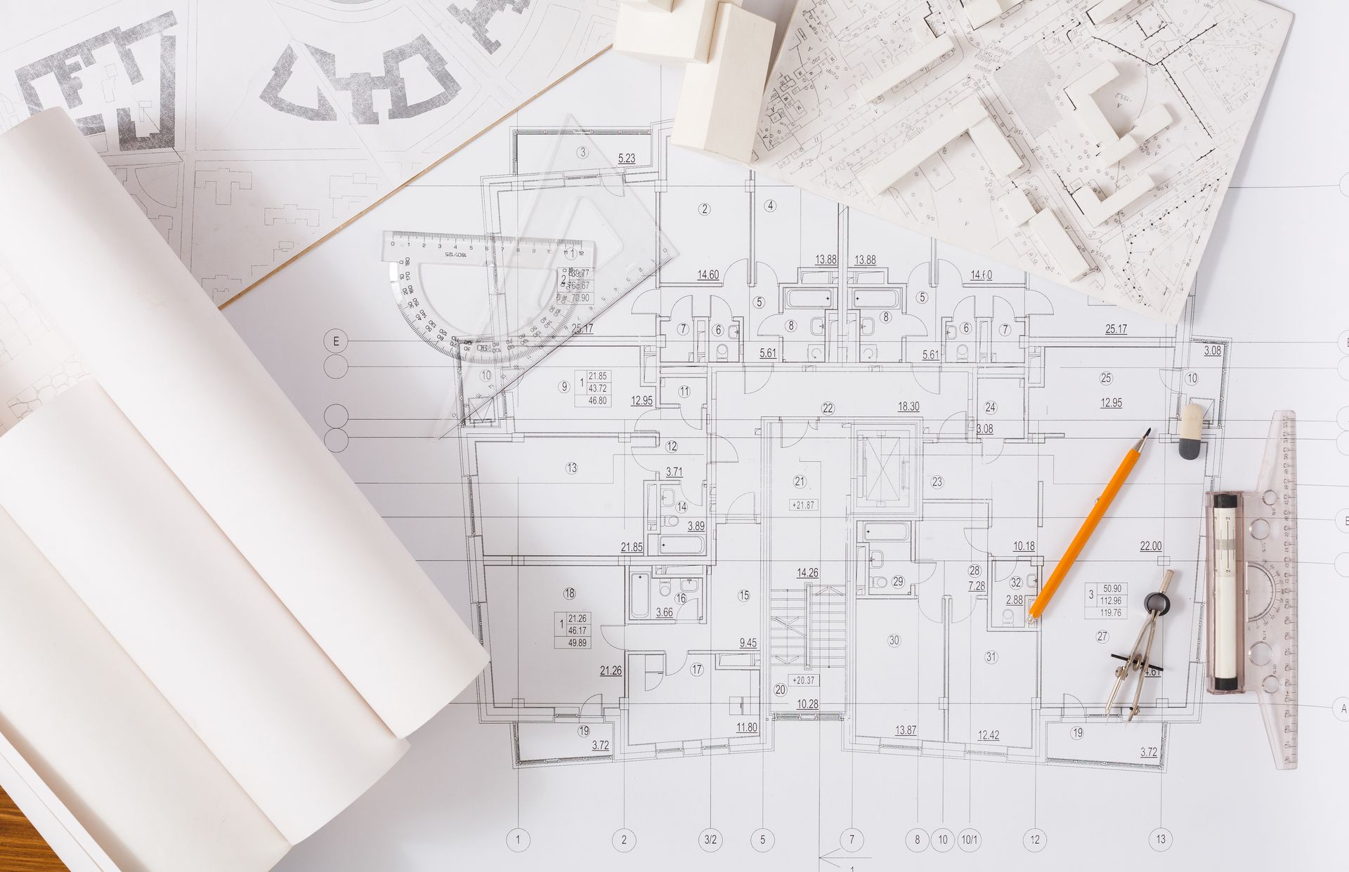 Plans architecturaux sur un bureau avec des rouleaux de papier, une règle et un crayon jaune.