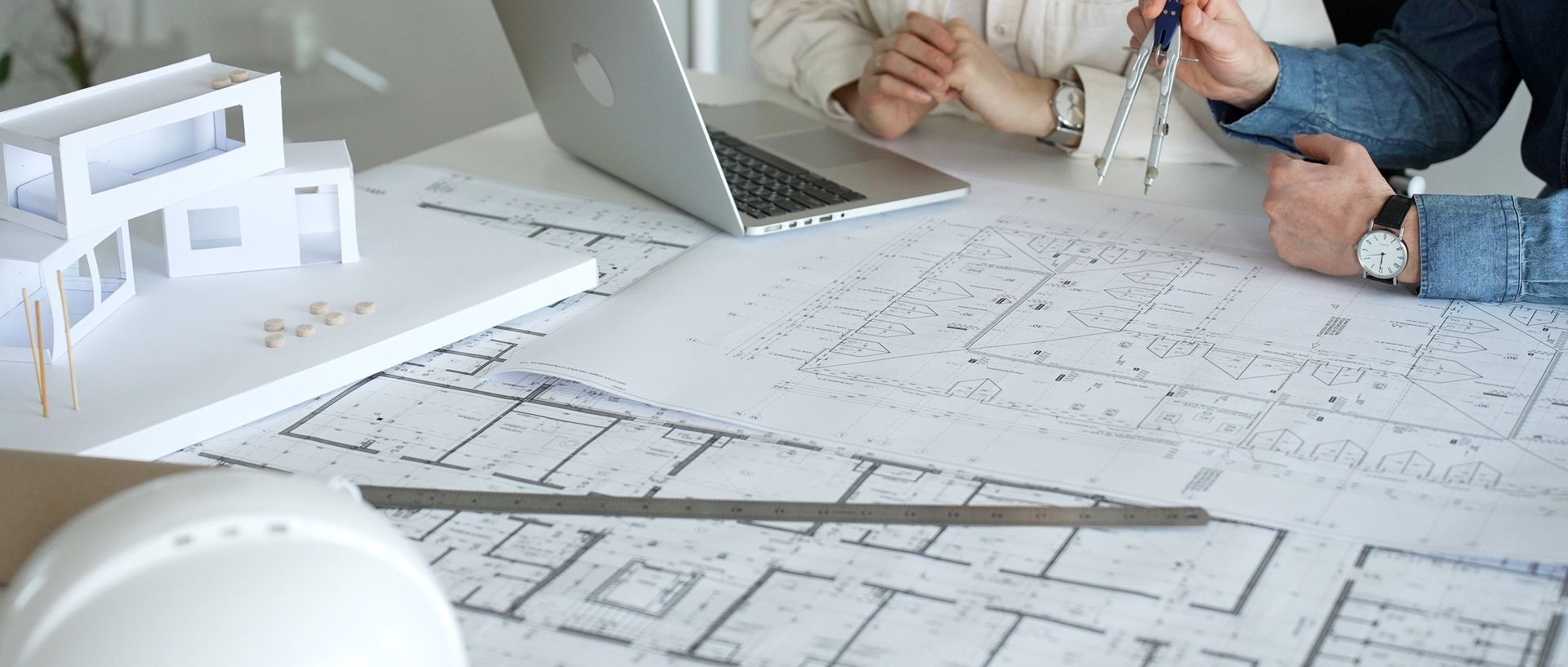 Des architectes examinent des plans et une maquette à l'échelle, assis à un bureau avec un ordinateur portable.