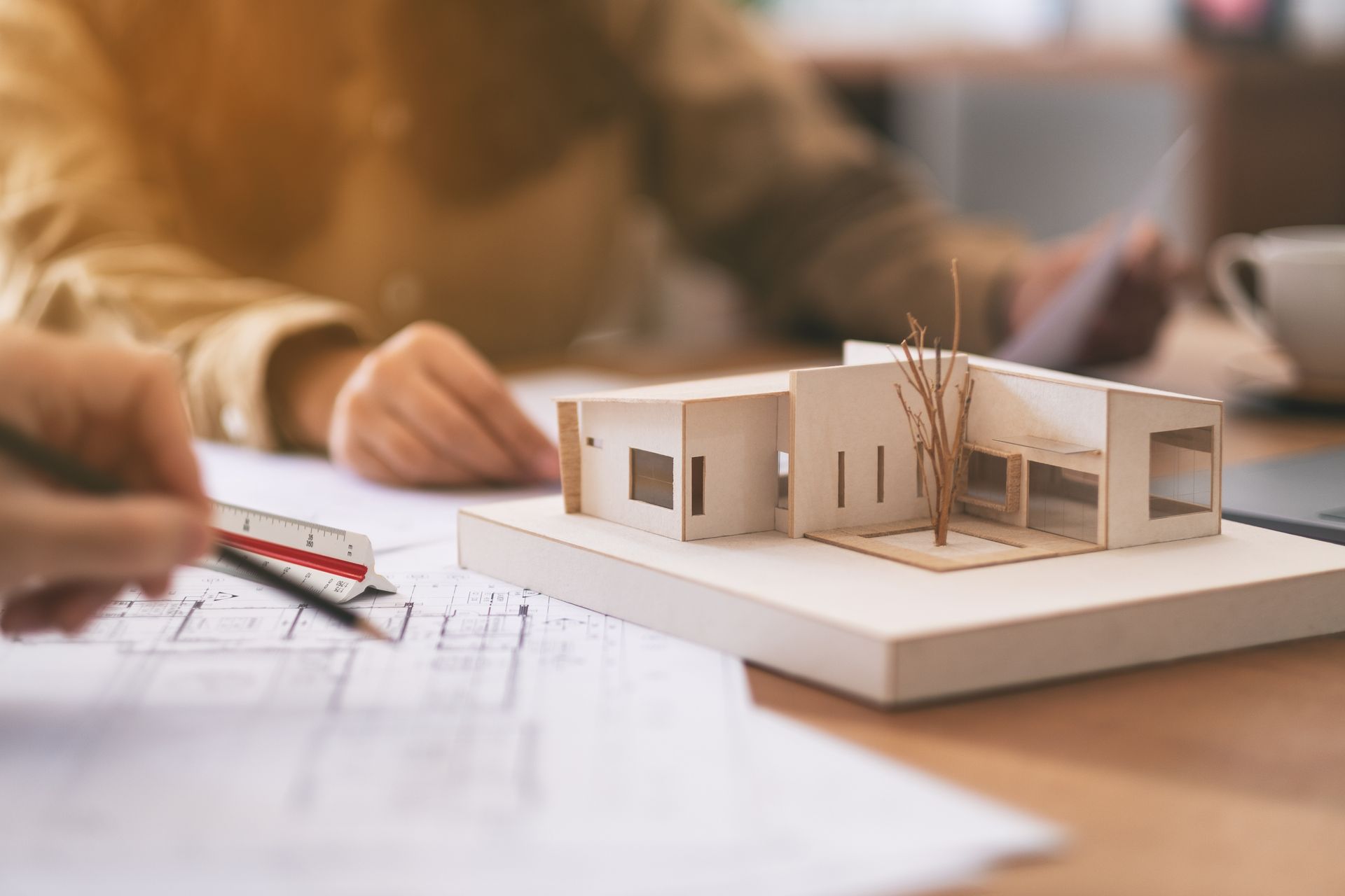 Des mains dessinent une maquette architecturale sur un bureau, avec des plans et des crayons.